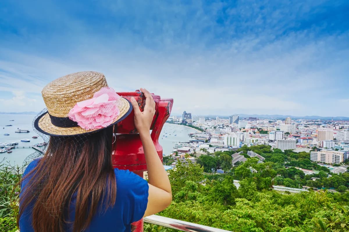 Woman tourist looking cityscape view through red binoculars from Pattaya view point